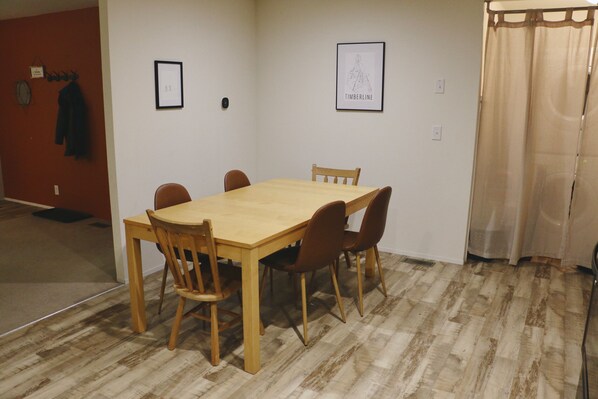 A dining area with a wooden table and chairs, a red wall with a coat rack, and a framed artwork on the wall.