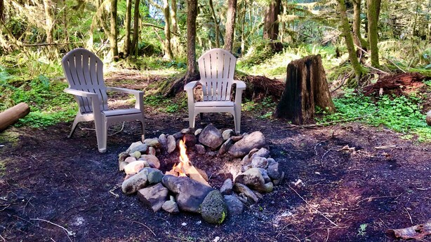 Dos sillas Adirondack alrededor de una fogata en un bosque.