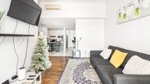 Een moderne woonkamer met een flatscreen-tv, een grijze bank met decoratieve kussens, een kamerbreed tapijt en een kleine kerstboom.