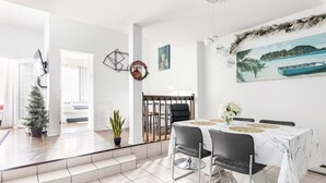 Een moderne eethoek met een witte tafel gedekt voor vier personen, een kerstboom en een schilderij met een strandthema aan de muur.