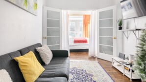 Een moderne woonkamer met een grijze bank, een kamerkleed met dessin, een bureau met computer en een televisie aan de muur.