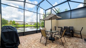 Un patio techado con una mesa, sillas, una parrilla y vistas a un lago y edificios al fondo.