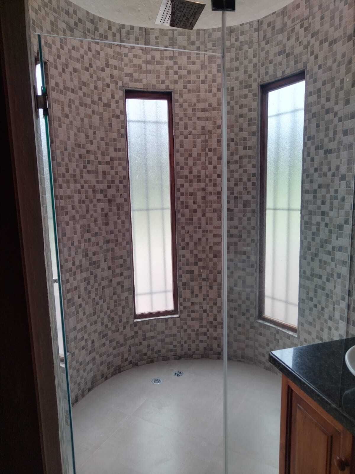 A bathroom with mosaic tile walls, two windows, a shower, and a sink.