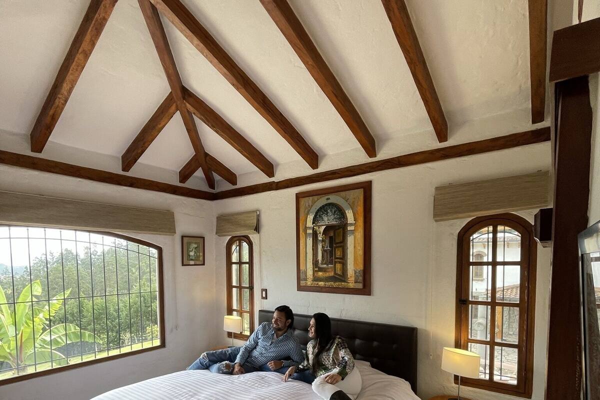Ein Schlafzimmer mit einem großen Bett, Holzbalken an der Decke und Blick ins Grüne.