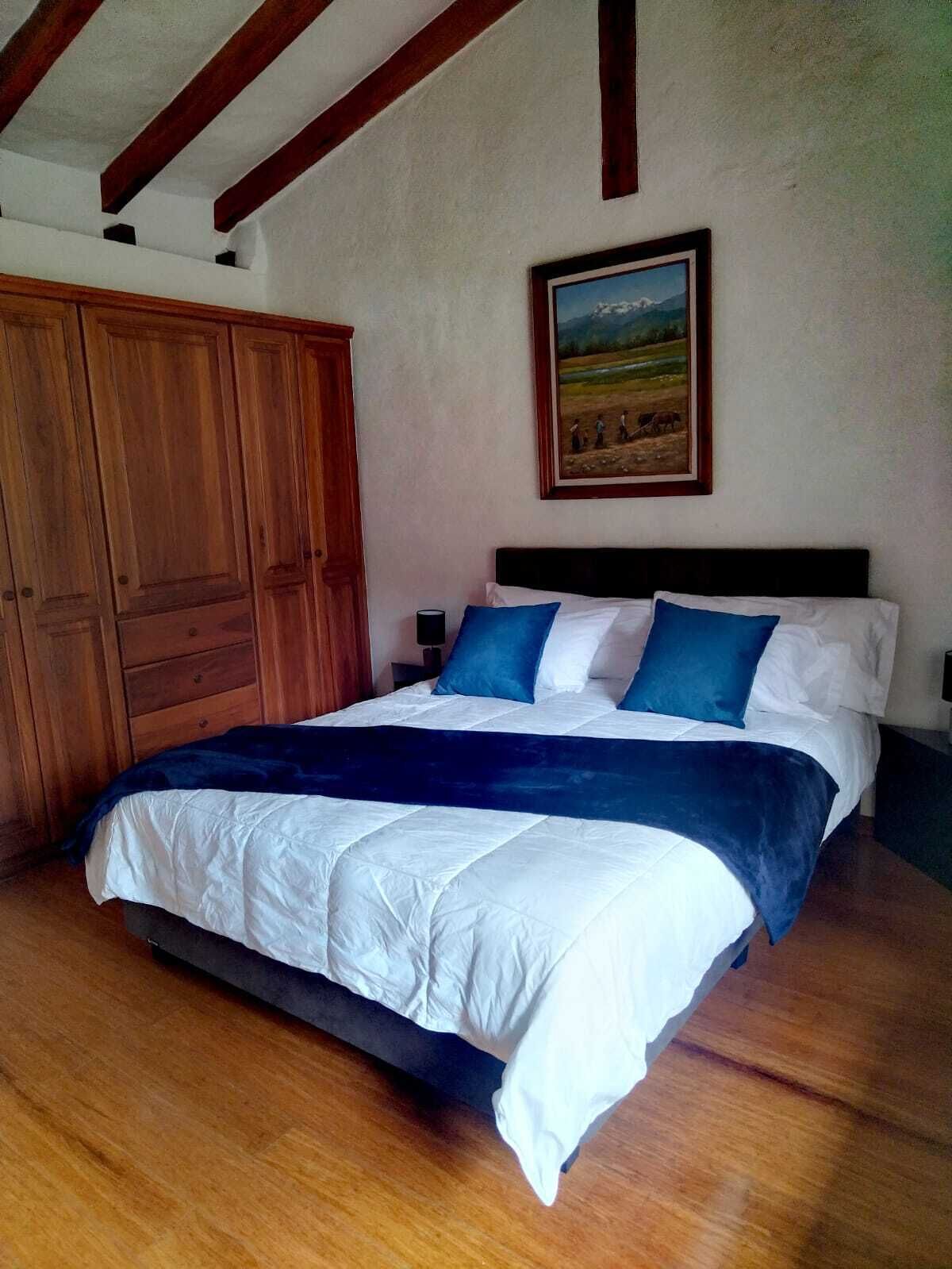 A bedroom with a large bed, wooden wardrobe, and a painting on the wall.