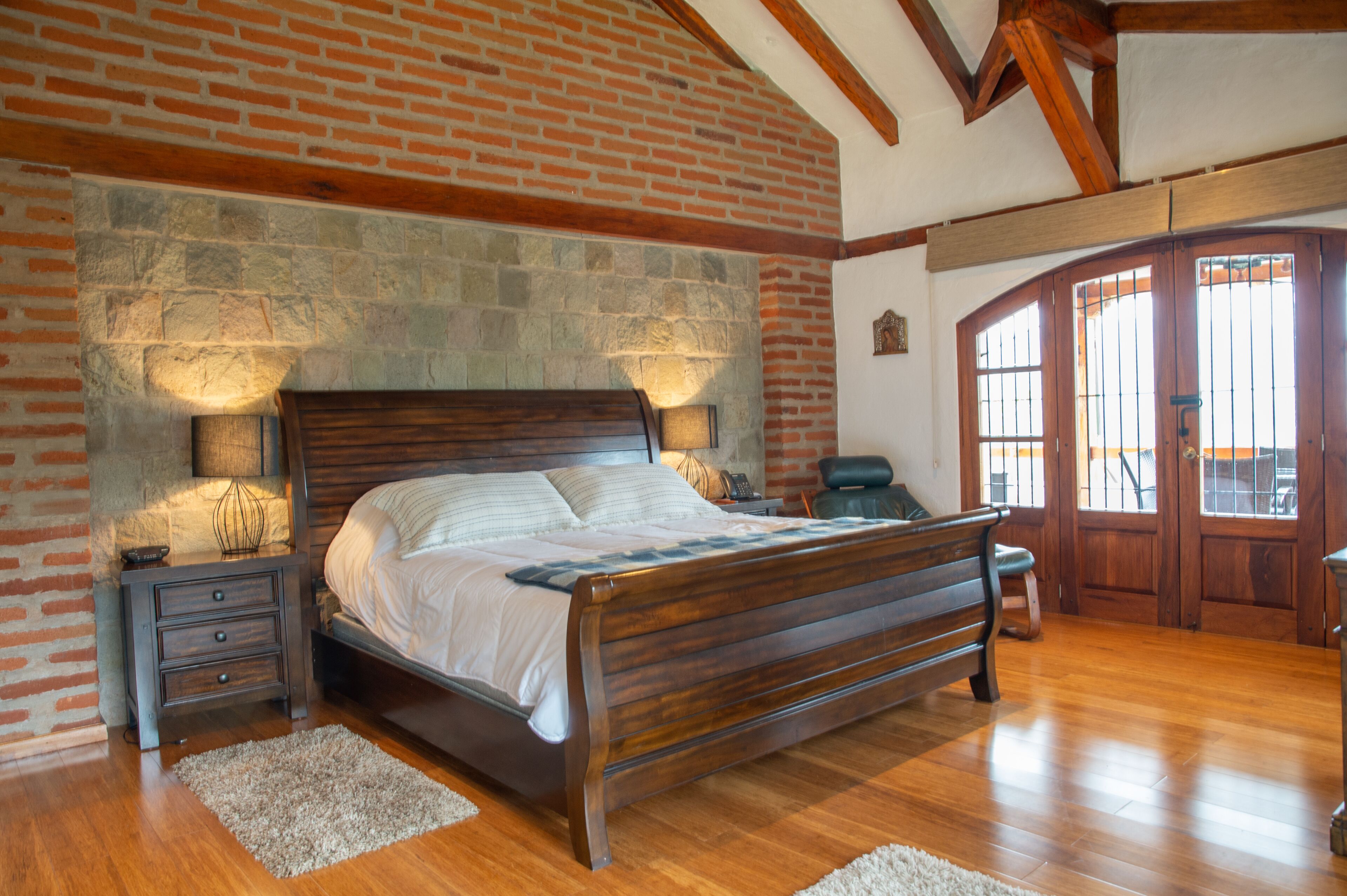 Un dormitorio con cama de madera, pared de piedra y suelo de madera.