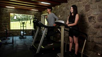 Un gimnasio con cintas de correr, una pared de piedra y una ventana con vista a un parque.