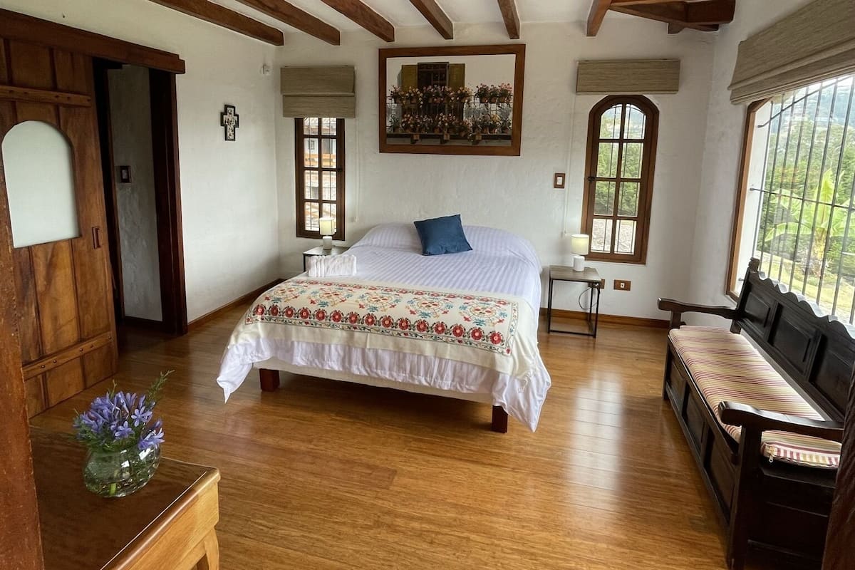 Ein geräumiges Schlafzimmer mit einem großen Bett, Holzbalken, einer Holzbank und einem kleinen Tisch mit Blumen in einer Vase.