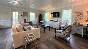 Un salon spacieux avec un canapé blanc, un fauteuil à motifs, une table basse et un téléviseur fixé au mur.