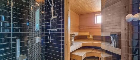 Une salle de bain moderne avec des murs recouverts de carreaux noirs, un espace douche et un plancher en bois.