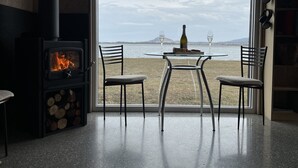 A room with a fireplace, a table with two chairs, and a view of the sea.