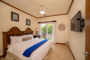 Una habitación de hotel con una cama grande, un ventilador de techo, un televisor montado en la pared y una ventana con cortinas.