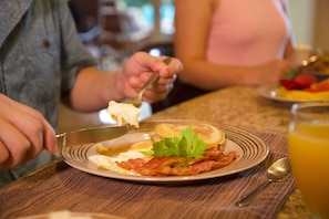 A breakfast setting with a plate of eggs, bacon, and toast, and a glass of orange juice on a wooden table.