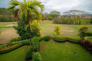 Un campo de golf bien cuidado con césped impecable, diversidad de árboles y una vista distante de una zona residencial.