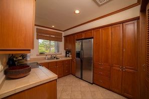 A kitchen with wooden cabinets, a stainless steel refrigerator, and a window with a view of greenery.
