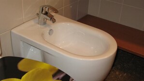 Un bidet blanc amb un aixeta cromada a un bany amb parets de rajola i un taulell de granit.
