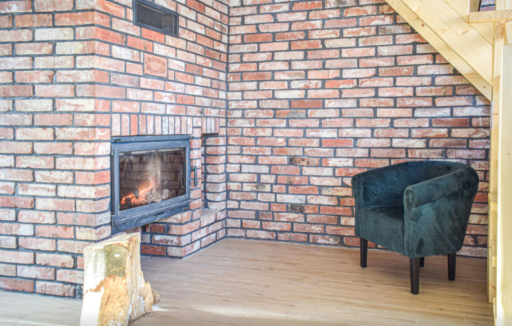 Una habitación de esquina con chimenea de ladrillo, un sillón oscuro y suelo de madera.
