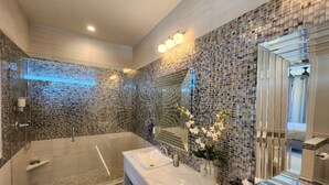 A modern bathroom with a glass-enclosed shower, a marble vanity, and a mosaic wall. - Two Bedroom Luxury Condo located in Beautiful February Point (George Town)