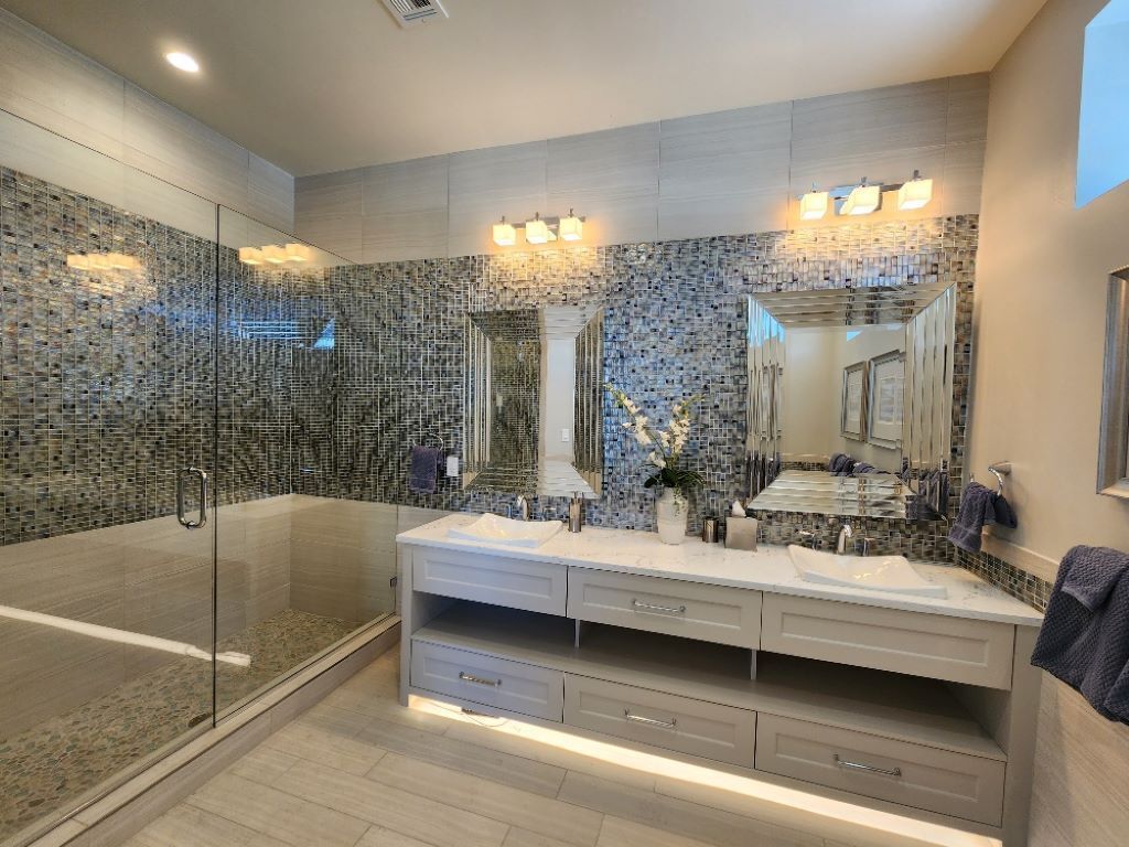 A modern bathroom with a glass-enclosed shower, a double vanity with a large mirror, and a mosaic tile backsplash.
