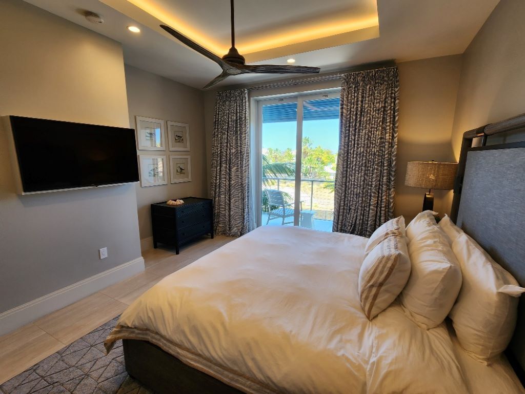 A modern bedroom with a large bed, ceiling fan, and a view of the outdoors.