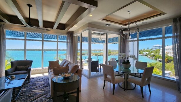 A spacious room with a large window offering a view of the sea. There is a seating area with a round table and chairs, and a sofa. - Two Bedroom Luxury Condo located in Beautiful February Point (George Town)