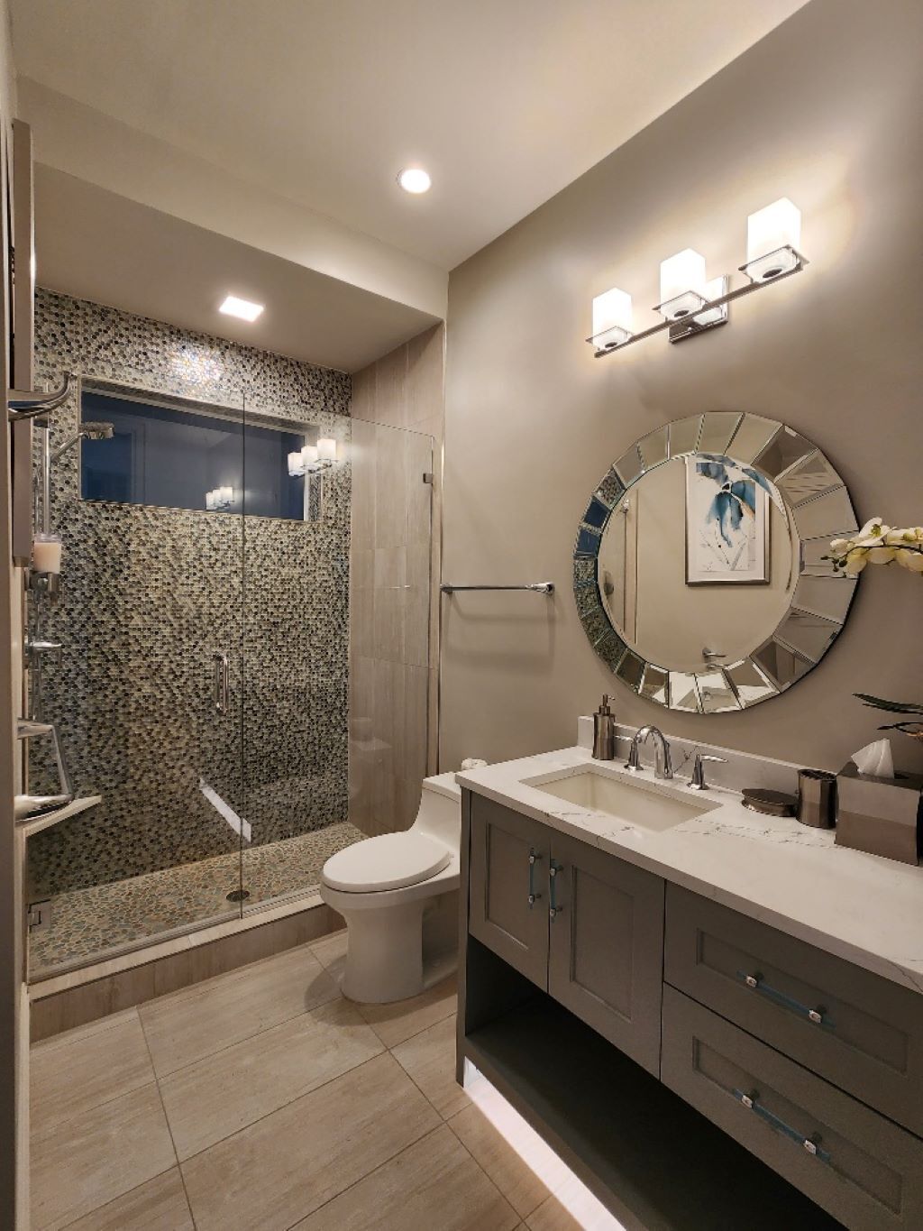 A modern bathroom with a glass-enclosed shower, a toilet, a vanity with a mirror, and a sink.