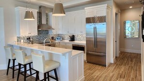 A modern kitchen with a central island, bar stools, pendant lighting, and a stainless steel refrigerator. - Two Bedroom Luxury Condo located in Beautiful February Point (Exuma)