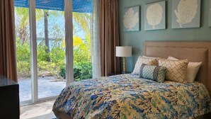 A bedroom with a large bed, a ceiling fan, and a view of greenery through the sliding glass door. - Two Bedroom Luxury Condo located in Beautiful February Point (Exuma)