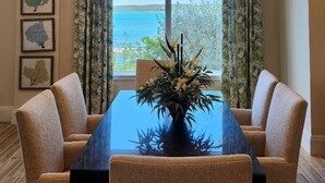 A dining area with a table and chairs, a hanging light fixture, and a view of the sea through large windows. - Two Bedroom Luxury Condo located in Beautiful February Point (Exuma)