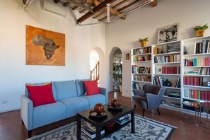 A living room with a sofa, coffee table, bookshelf, and a painting on the wall.