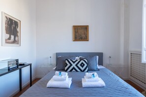 A bedroom with a bed, pillows, a bedside table, a radiator, and a framed picture on the wall.