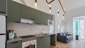 Eine moderne Küche mit grünen Schränken, einer Mikrowelle und einem Spülbecken. Im angrenzenden Wohnbereich befindet sich ein Holzboden und ein graues Sofa.