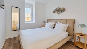 Ein Schlafzimmer mit einem großen Bett, einem Spiegel, einem Wandbild und einem Fenster mit Blick auf Gebäude.