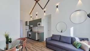 Ein zeitgemäßer Wohnbereich mit einem Glastisch, einem grauen Sofa und einer Küchenzeile mit einer Mikrowelle.