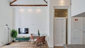 Ein modernes Wohnzimmer mit Holzboden, einem grünen Sofa, einem Fernseher und einem Essbereich mit zwei Stühlen und einem Tisch.