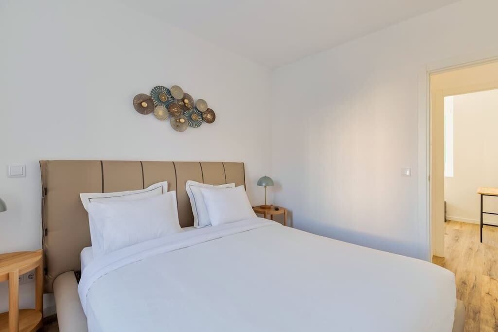 Un lit bien fait, avec du linge de lit blanc, une tête de lit en bois et un élément décoratif fixé au mur au-dessus.