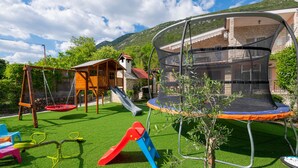 Ein Garten mit einem Holz-Spielhaus, einer Rutsche, einem Trampolin und einer Schaukel.