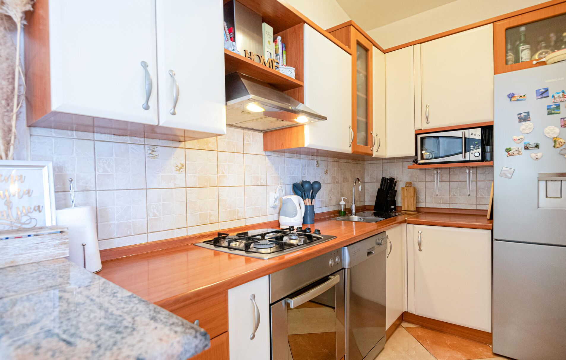Een keuken met witte kastjes, een gasfornuis, een magnetron en een koelkast.