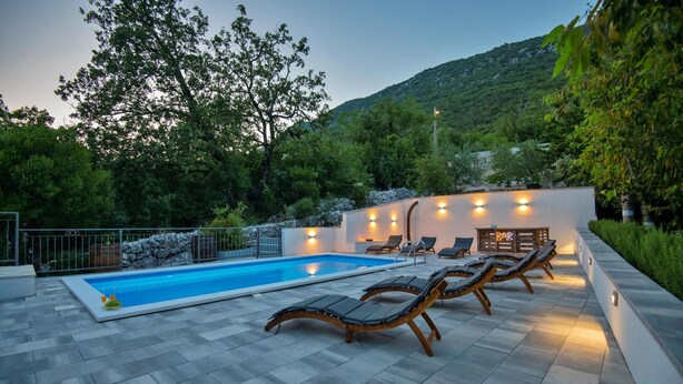 Ein Pool mit Liegestühlen und Barbereich, umgeben von Bäumen und einem Berg im Hintergrund.