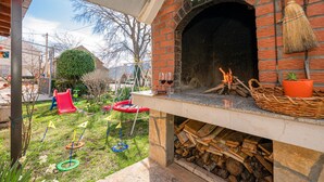 A brick oven with a fire burning inside, surrounded by a garden with a swing set and a small pond. - Lovely home in Vrgorac (Vrgorac)
