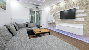 Ein modernes Wohnzimmer mit einem Ecksofa, einem Couchtisch und einem Flachbildfernseher, der an einer strukturierten Wand angebracht ist.
