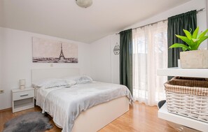A bedroom with a bed, a bedside table, a lamp, a framed picture of the Eiffel Tower, a potted plant, and a wicker basket. - Lovely home in Vrgorac (Vrgorac)
