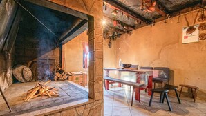 Ein rustikales Interieur mit Kamin aus Stein, Holzscheiten, einem Esstisch mit Stühlen und einem Kalender an der Wand.