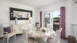 A dining area with a glass table surrounded by cushioned chairs, a white cabinet with drawers, a vase with dried flowers, and a large mirror on the wall. - Casa Palm House - private pool in Carvoeiro (Carvoeiro)