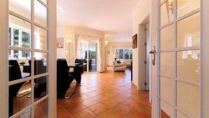 Uma sala de estar ampla, com uma mesa de jantar e cadeiras, um sofá e vista através de grandes portas de vidro.