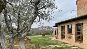 Edificio de piedra con techo de ladrillo, jardín con un árbol y vista a una colina al fondo.