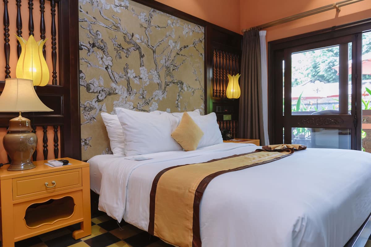 Una camera d'albergo con un letto, un comodino, una lampada e una finestra vista verde.