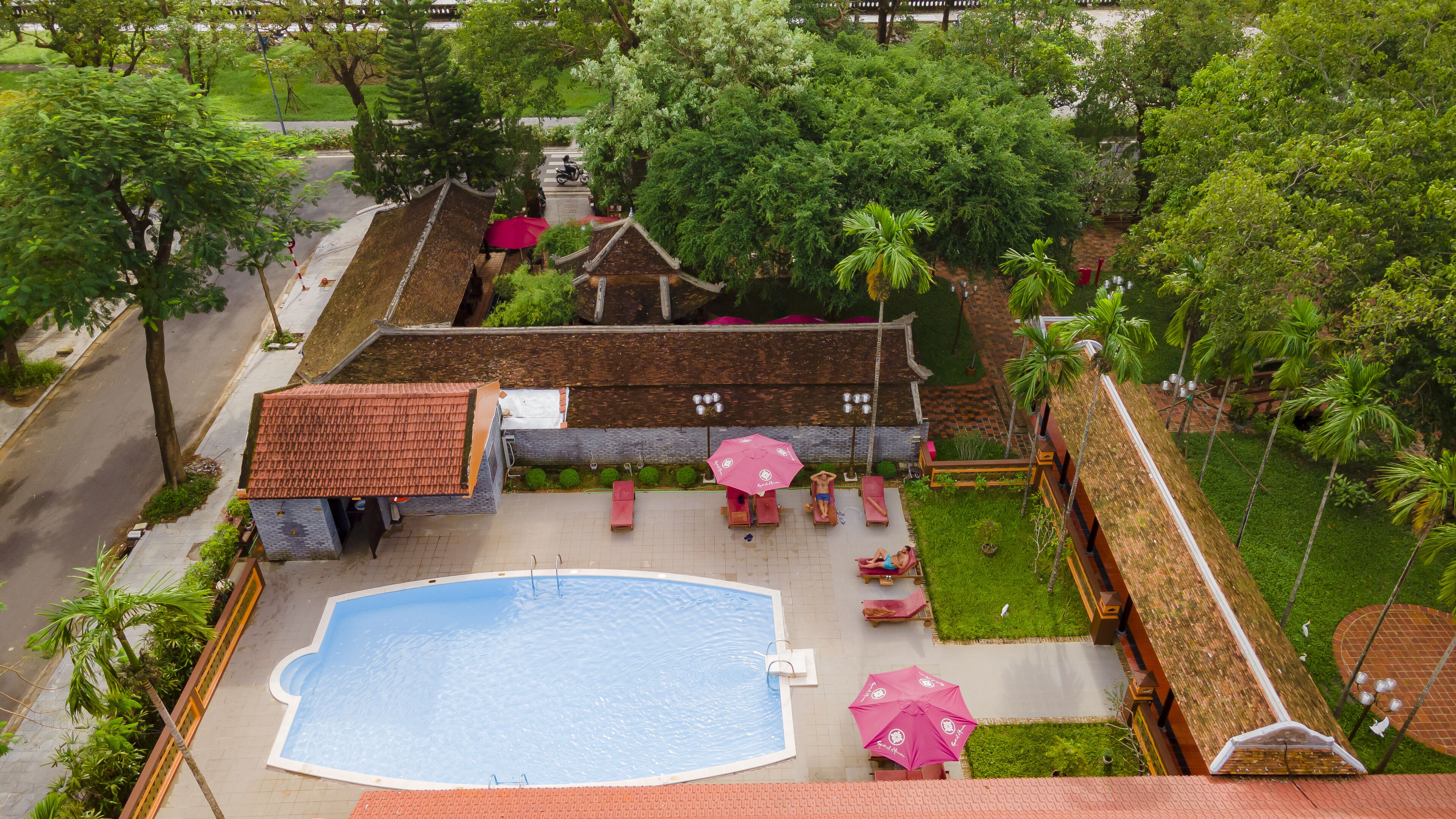 An aerial view of a resort with a swimming pool, lounge chairs, and umbrellas.