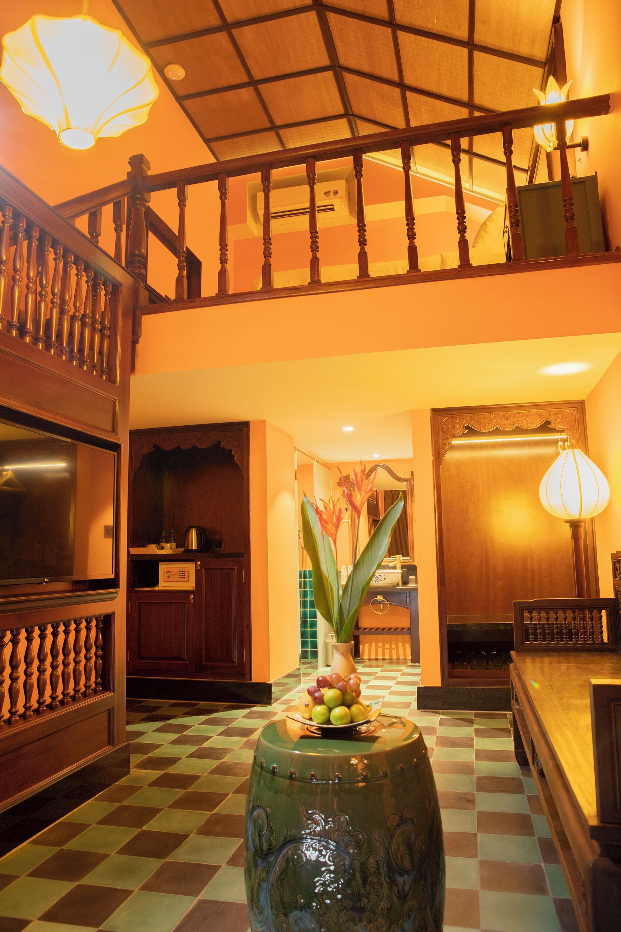 A spacious lobby with a checkered floor, a wooden staircase, and a large vase with flowers.