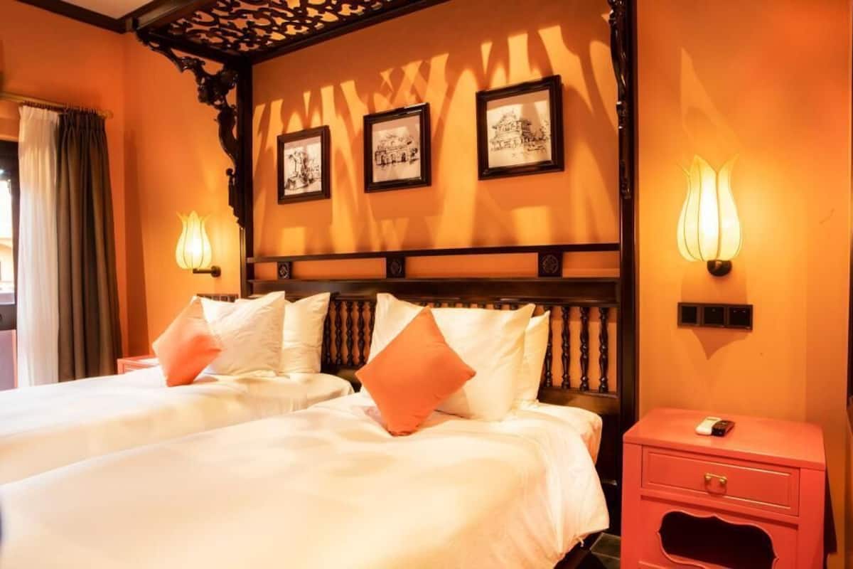 Camera d'albergo con due letti, un comodino, una lampada e quadri appesi al muro.